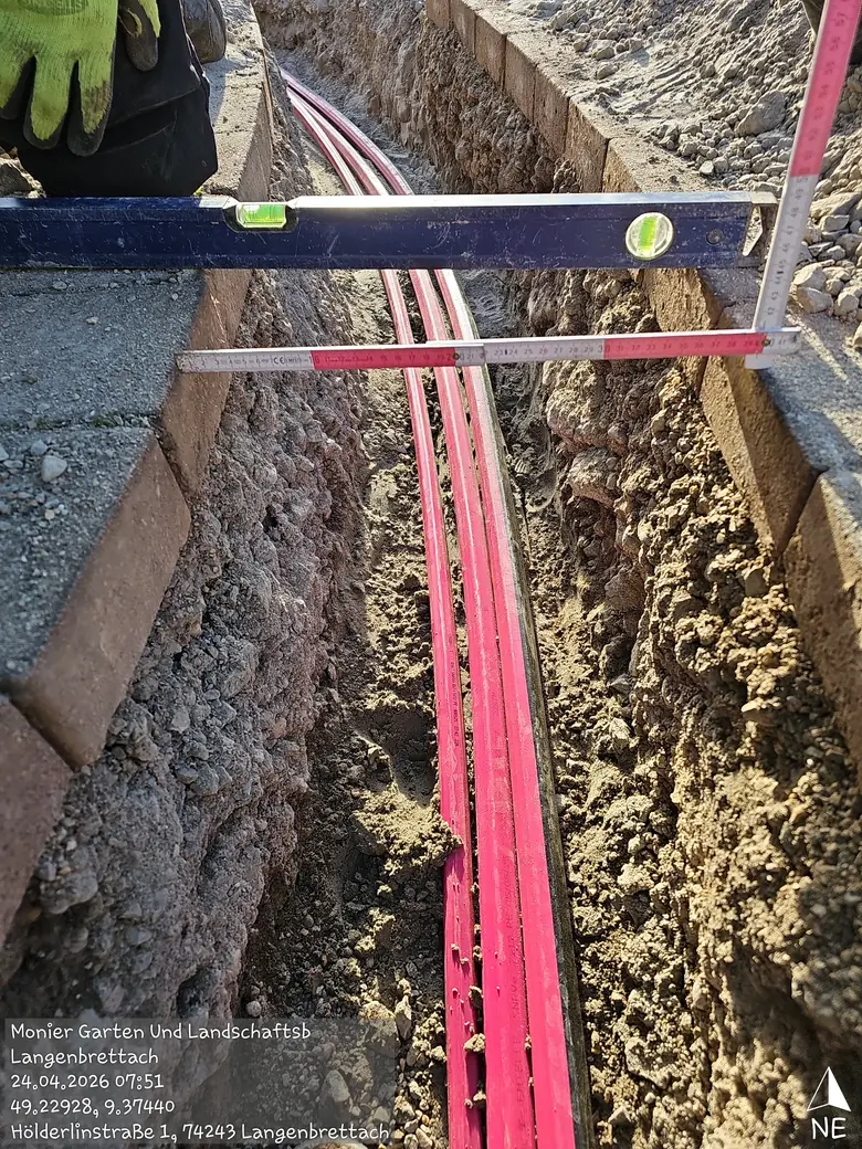 Leitungsgraben mit verlegten Leerrohren, Höhenkontrolle mit Wasserwaage und Zollstock