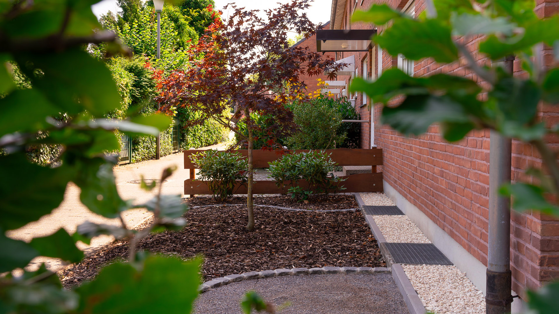 Ein grüner Garten mit bunten Bäumen und roten Ziegelwänden im Hintergrund.