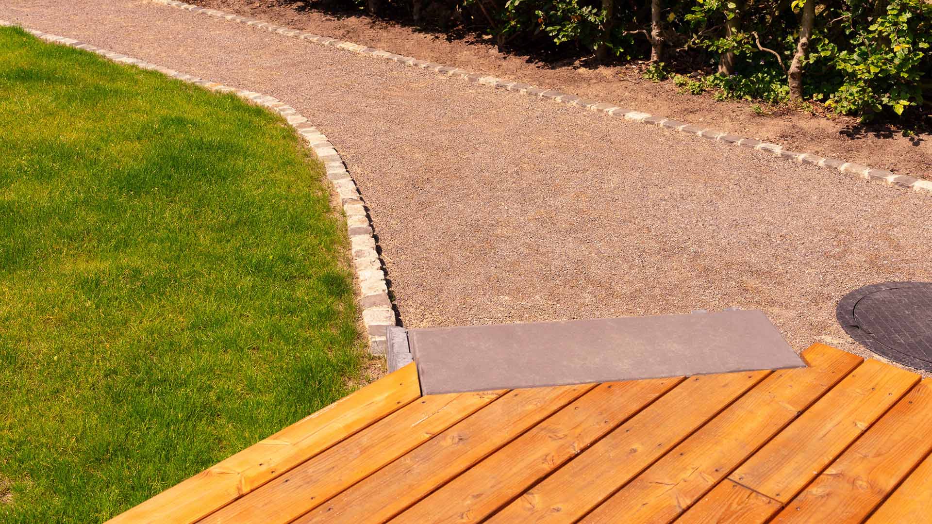 Holzterrasse, grüner Rasen, Kiesweg, sonniger Tag, harmonische Gartenansicht.