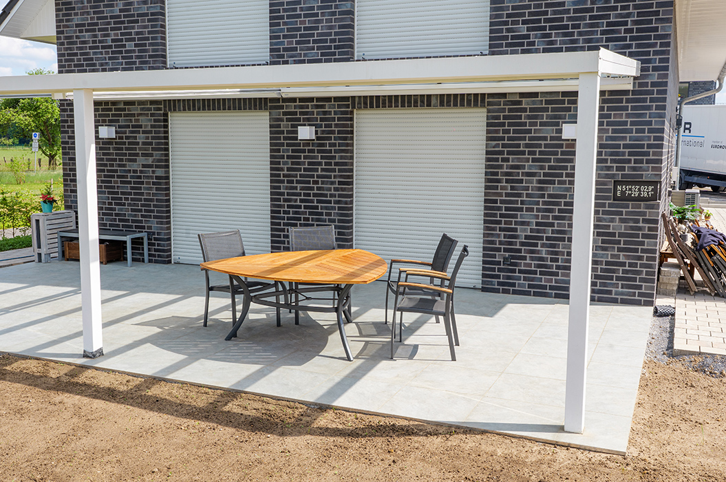 Überdachte Terrasse mit Holztisch und vier Stühlen vor einem modernen Ziegelhaus.