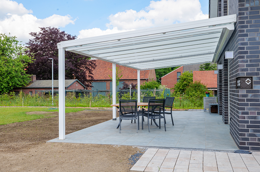 Überdachte Terrasse mit Tisch und Stühlen, umgeben von grünen Bäumen und roten Ziegeldächern.
