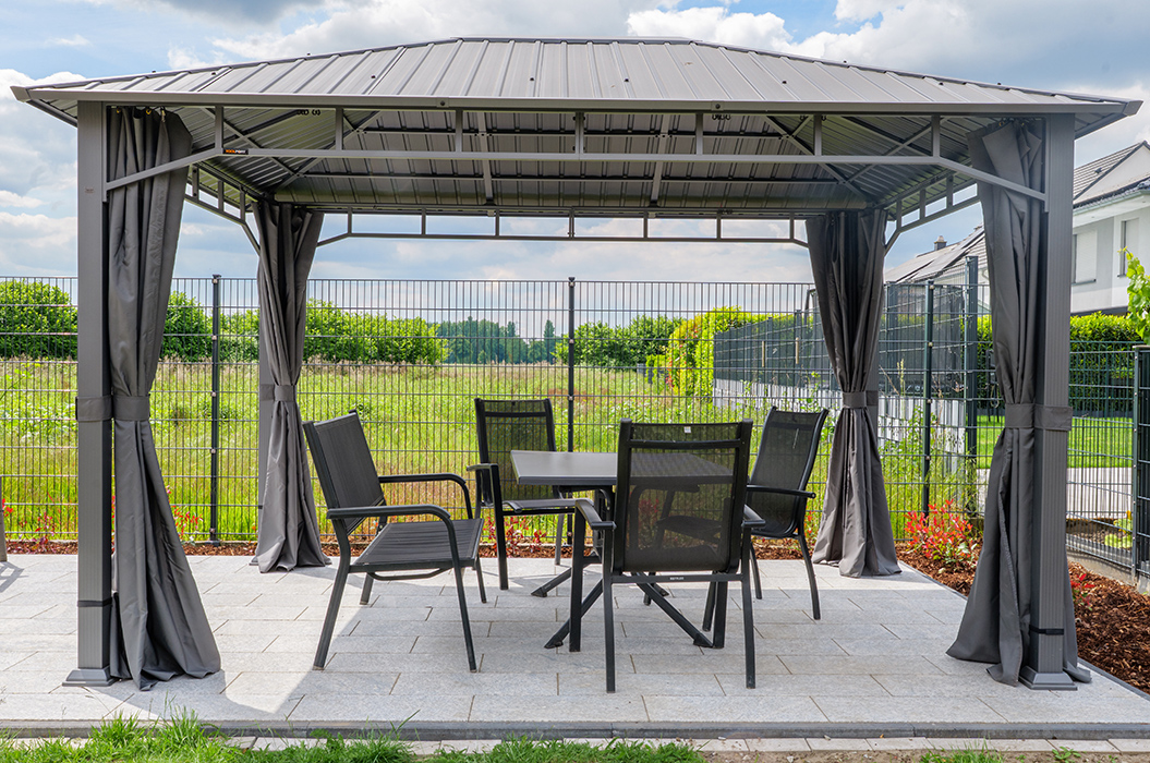 Gartenpavillon mit Metallstruktur, darunter fünf schwarze Stühle und ein Tisch auf Steinplatten.