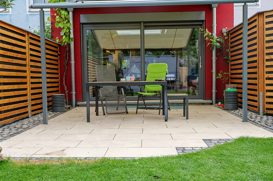 Ein moderner Garten mit Tisch, zwei Stühlen, roten Wänden und Holzlattenzäunen.