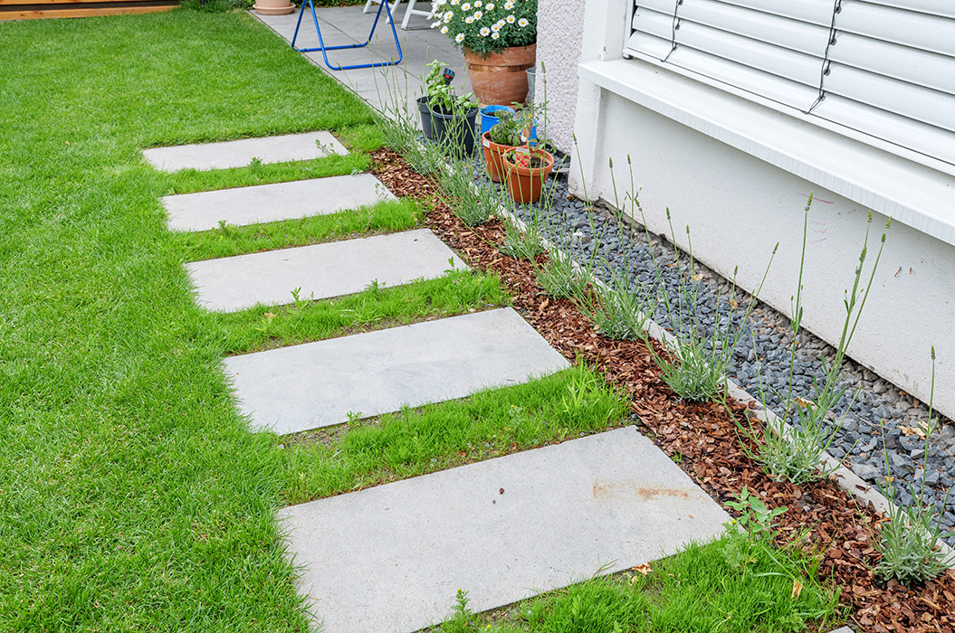 Grüner Garten mit Steinpfad, Lavendel, Kies und weißen Fensterläden.