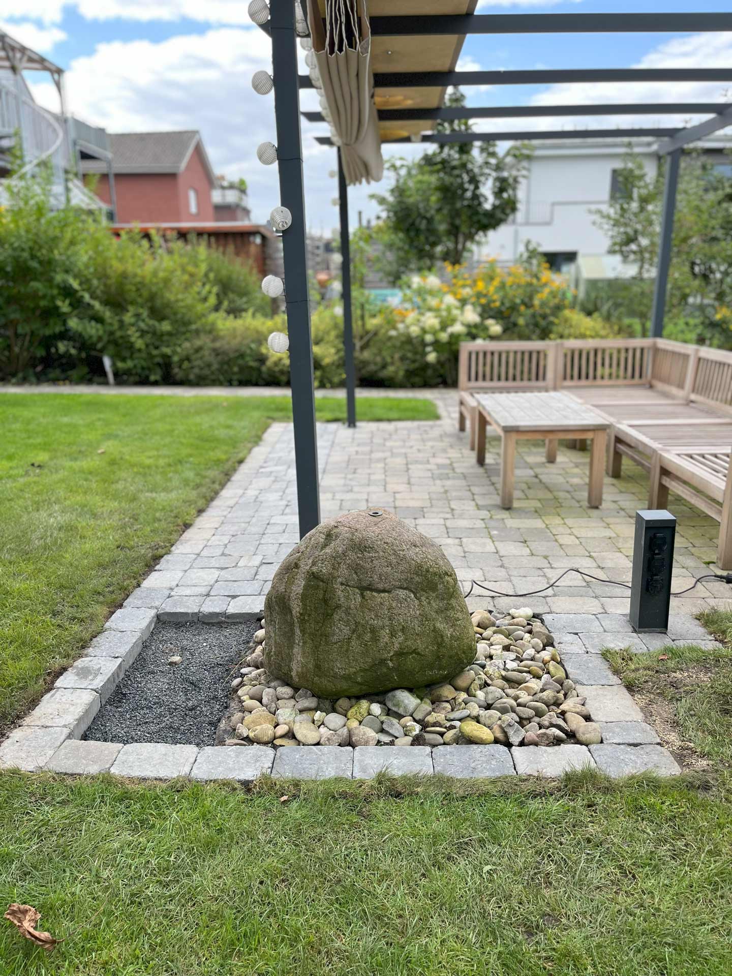 Großer Felsbrocken auf einem Kiesbett in einem Garten mit Rasen und Sitzbereich