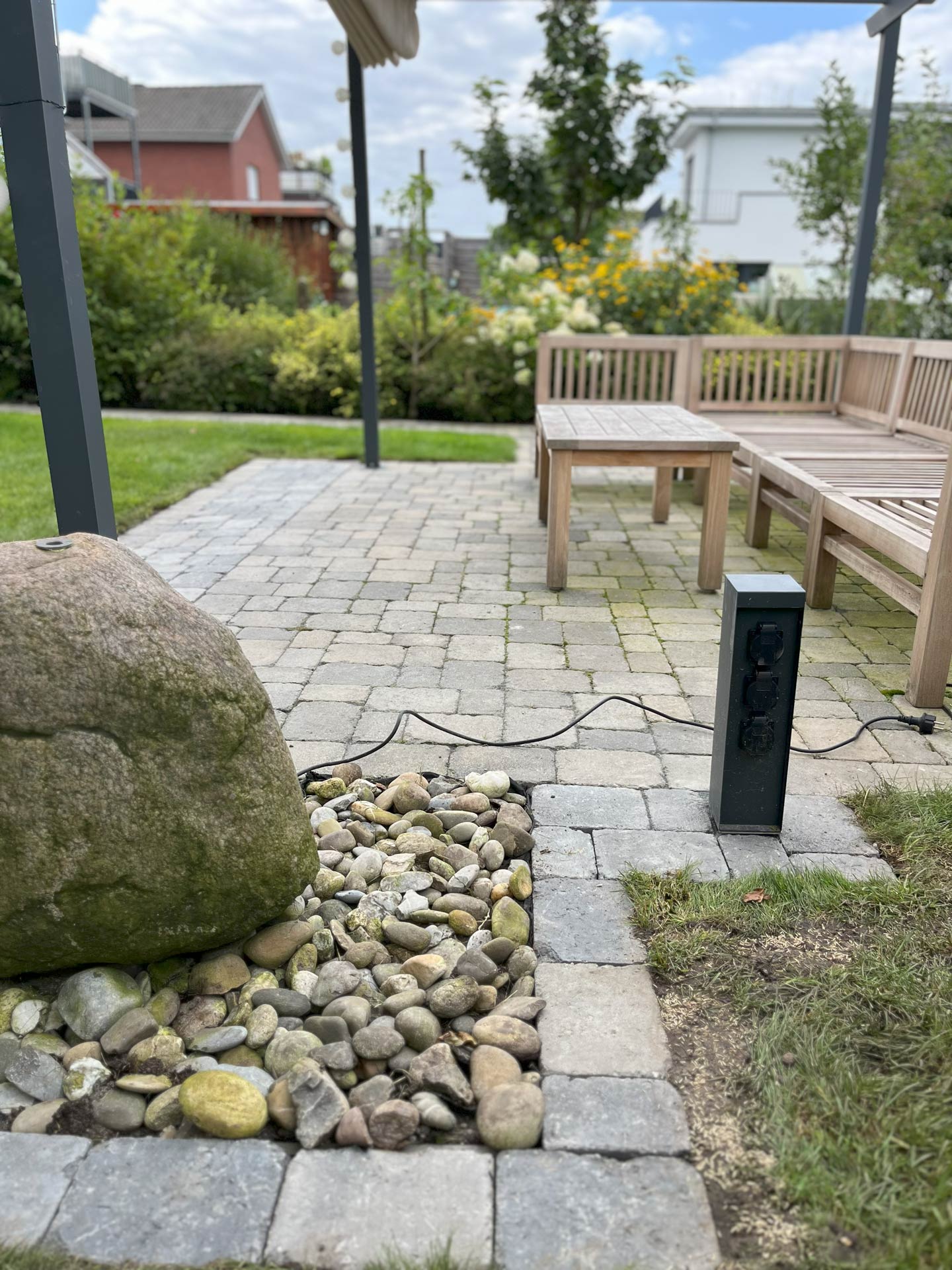 Eine gepflasterte Terrasse mit Holzbänken, Gartenblick und Steckdose.