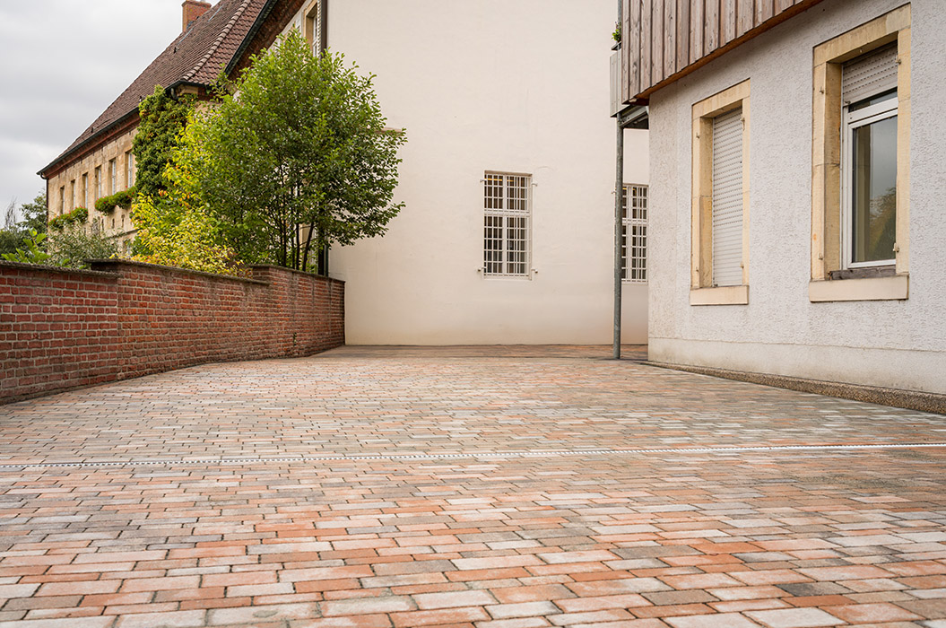 Ein leerer gepflasterter Hof mit roten und beigen Steinen neben hellen Gebäuden