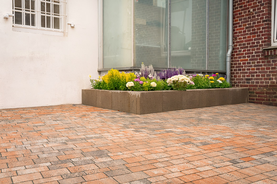 Ein Beet mit bunten Blumen neben einer Backsteinwand auf gepflastertem Boden