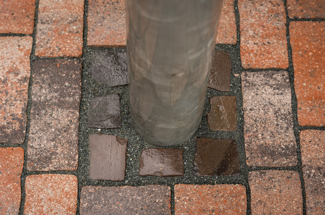 Ein silberner Metallpfosten steht auf nassen rötlichbraunen Kopfsteinpflastersteinen
