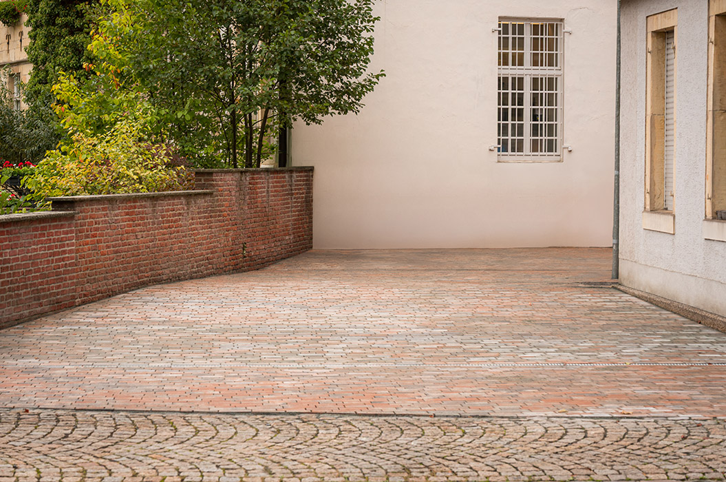 Ein leerer gepflasterter Innenhof mit einer roten Backsteinmauer und grünen Bäumen