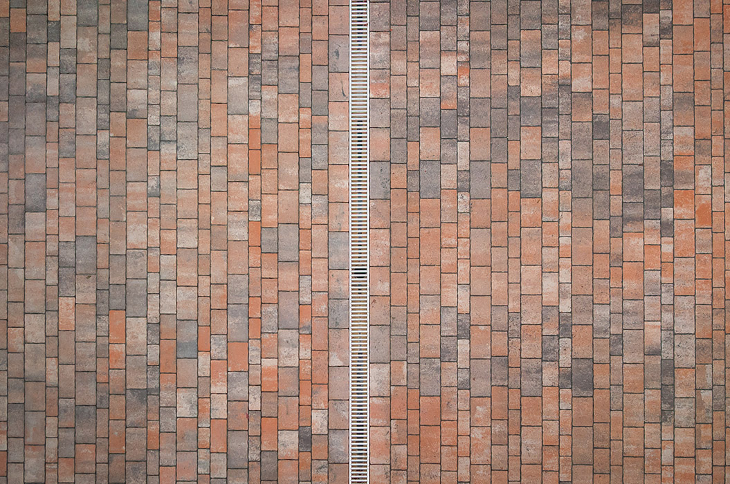 Backsteinmuster in warmen Rottönen mit einem weißen Abflussgitter in der Mitte