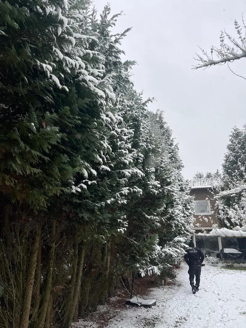 Person in dunkler Jacke mit neutralem Blick im verschneiten Waldweg