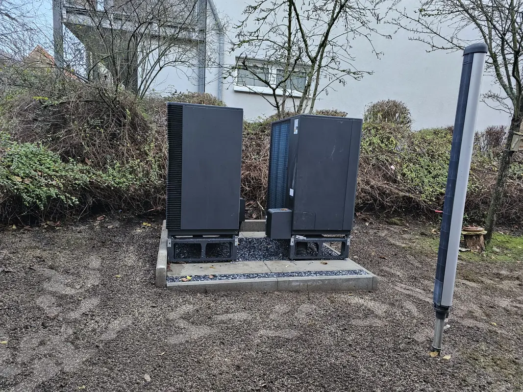Zwei schwarze Technikschraenke auf Betonplatte im kahlen Garten, neutral