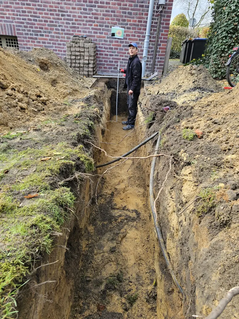 Mann mit ernstem Blick in schwarzer Kleidung im Sandgraben mit Kabeln
