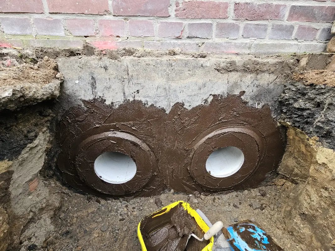 Zwei weiße Rohre in brauner Wandabdichtung, Baustelle mit Ziegeln und Eimer