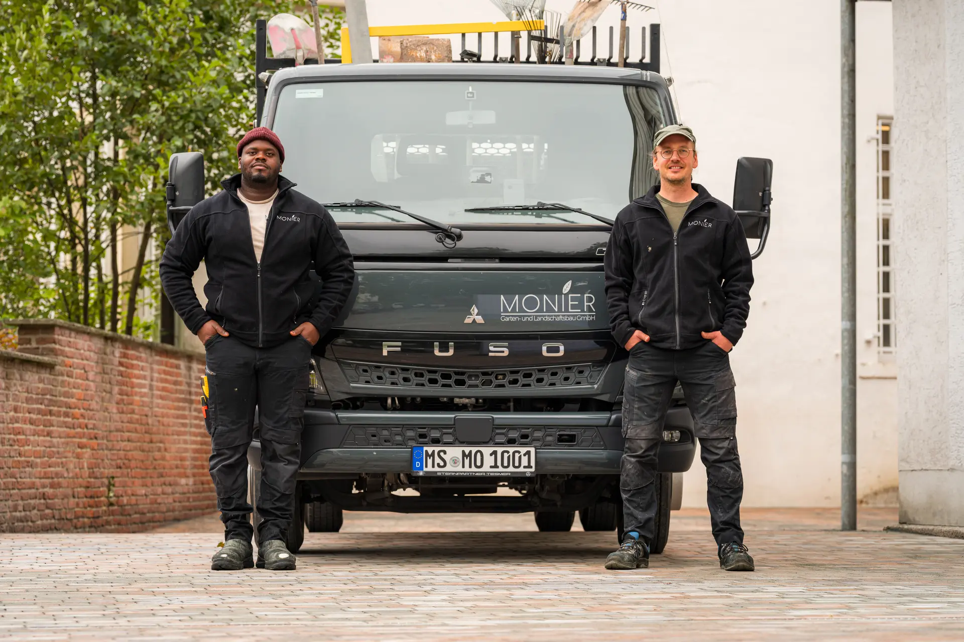 Zwei Maenner laecheln vor schwarzem Lkw mit Monier Logo und Gabeln