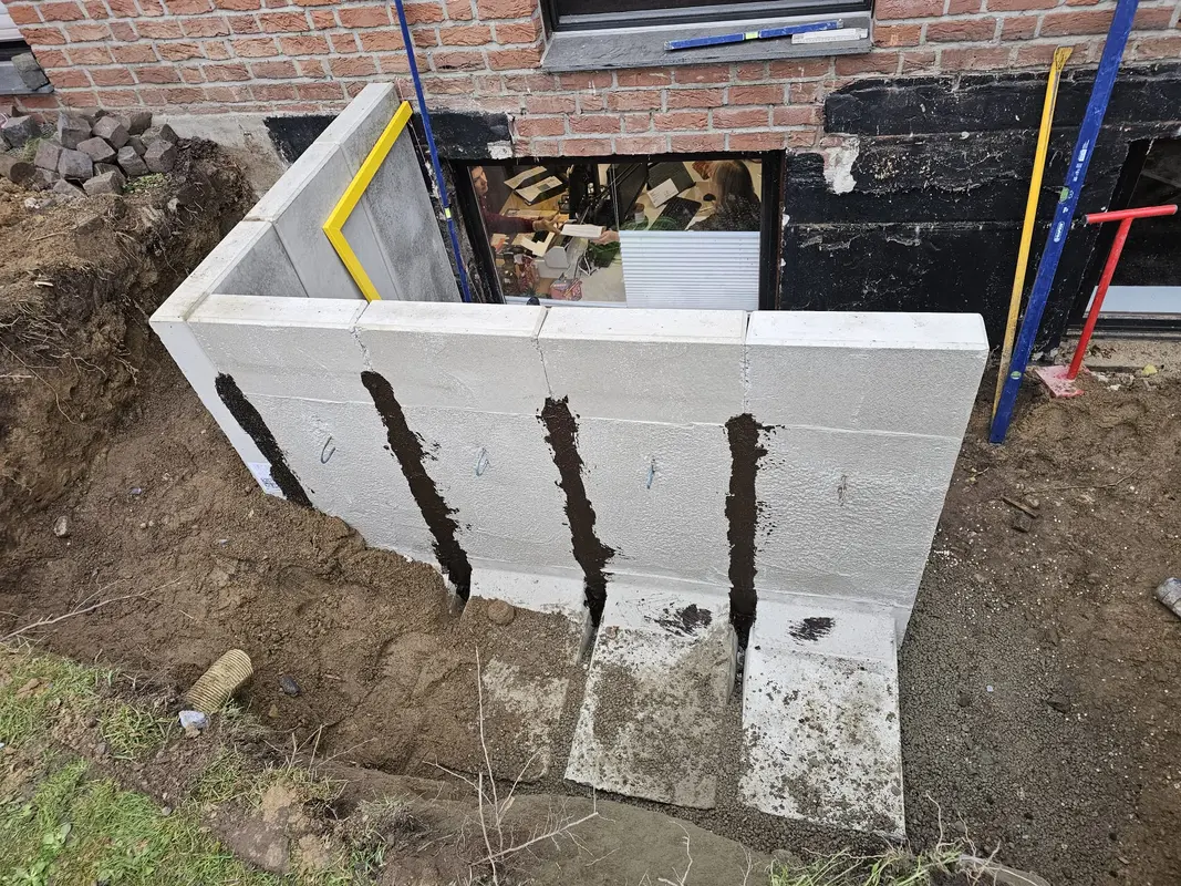 Weiße Betonmauer am Kellerfenster mit schwarzen Streifen und Erdgraben