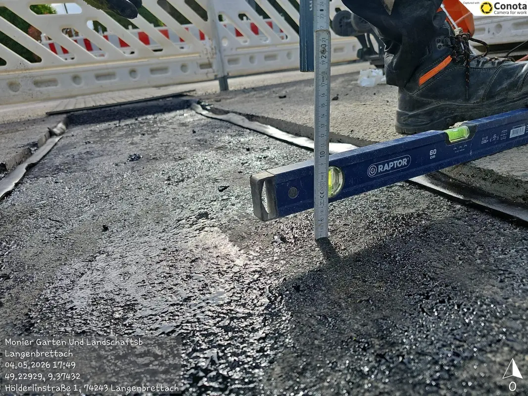 Arbeiterstiefel auf schwarzem Asphalt neben blauem Raptor Niveau und Zollstock