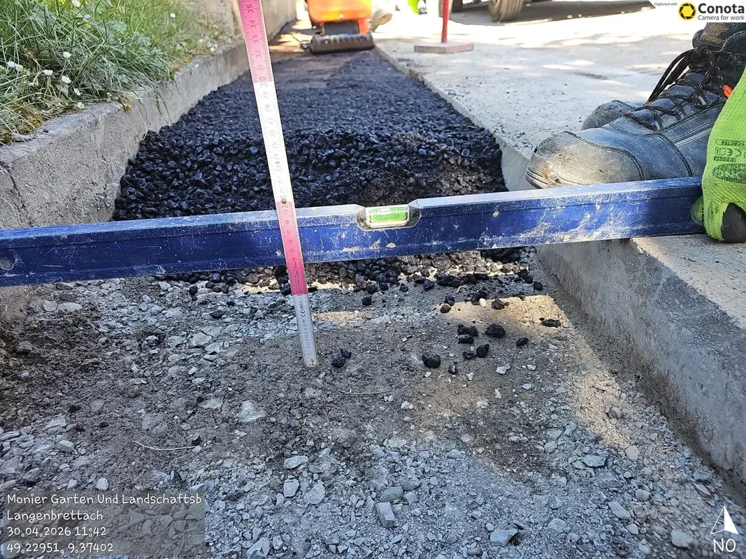 Arbeiterstiefel neben blauem Richtscheit auf schwarzem Asphaltbett, neutral