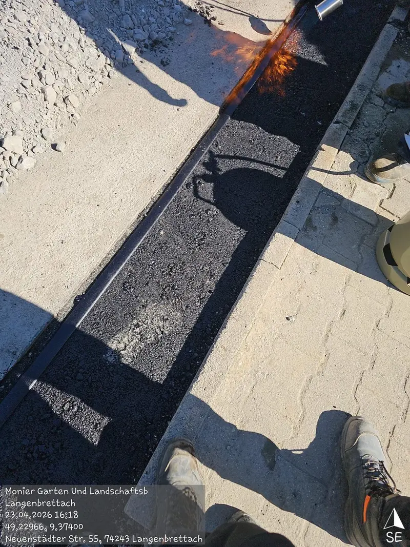 Arbeiter, konzentriert, gießt heißes Bitumen in Rinne, dunkler Asphalt, Flamme